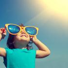 Happy little girl with big sunglasses looking at the sun
